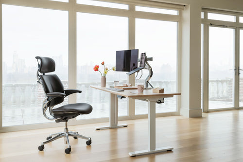 Support d'ordinateur portable Humanscale NH1 monté sur un bras, à côté de deux écrans