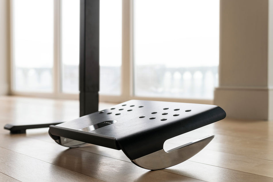 Repose-pieds à bascule Humanscale FR500 noir au pied d'un poste de travail